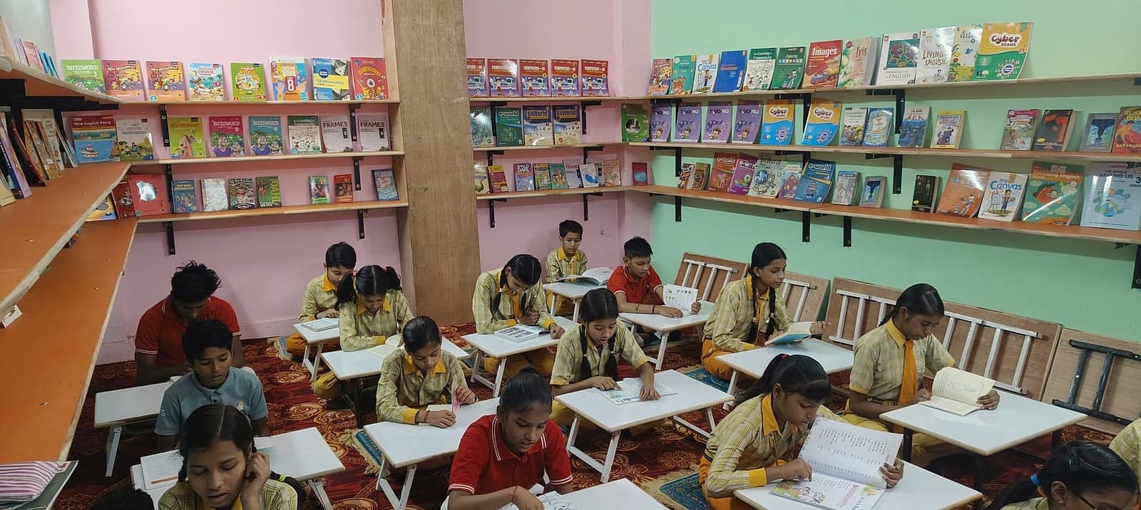 Students working at low desks in the learning centre library, shelves of books behind them